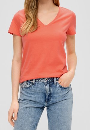 Koralowa koszulka typu V-neck z krótkimi rękawami, wykonana z miękkiego materiału, w połączeniu z niebieskimi dżinsami o wysokim stanie, o klasycznym kroju.