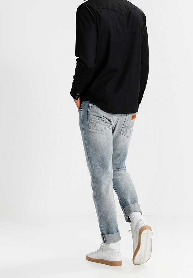 Camisa negra de manga larga con puños abotonados, combinada con jeans de mezclilla azul claro. Calcetines blancos y zapatillas altas con suela color beige.