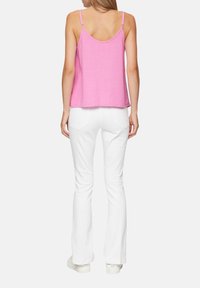 Růžový top bez rukávů s texturovanou látkou zkombinovaný s bílými širšími kalhotami. Top má tenké ramínka a volný střih.