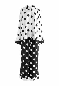 Čiernobiely outfit s bodkami, obsahujúci blúzku s dlhým rukávom a gombíkmi a zodpovedajúce široké nohavice, s kontrastným lemovaním na manžetách a spodnom okraji.