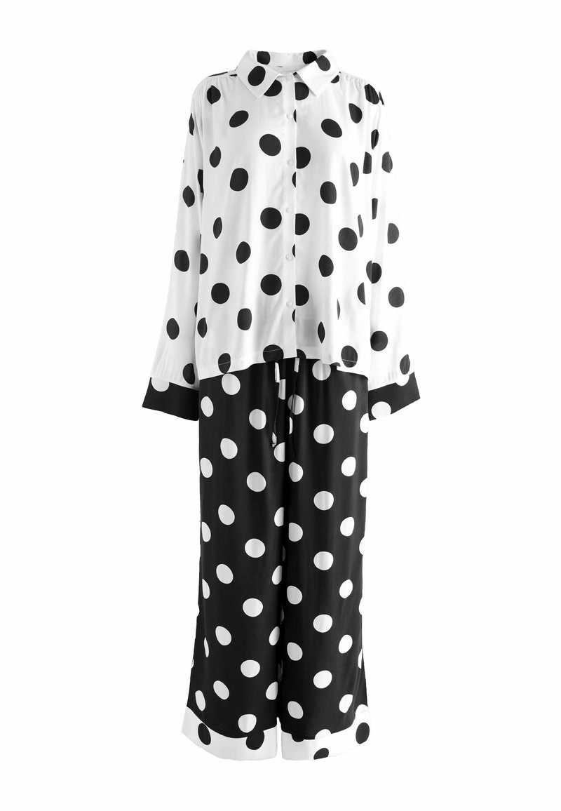Čiernobiely outfit s bodkami, obsahujúci blúzku s dlhým rukávom a gombíkmi a zodpovedajúce široké nohavice, s kontrastným lemovaním na manžetách a spodnom okraji.