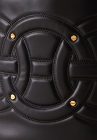 Black leather handbag featuring a quilted design with circular patterns and gold-tone hardware accents. Smooth texture with detailed stitching.