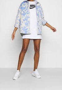 Giacca in fleece a motivo blu chiaro e crema sopra una maglietta Nike bianca, abbinata a un vestito mini bianco e sneakers bianche.