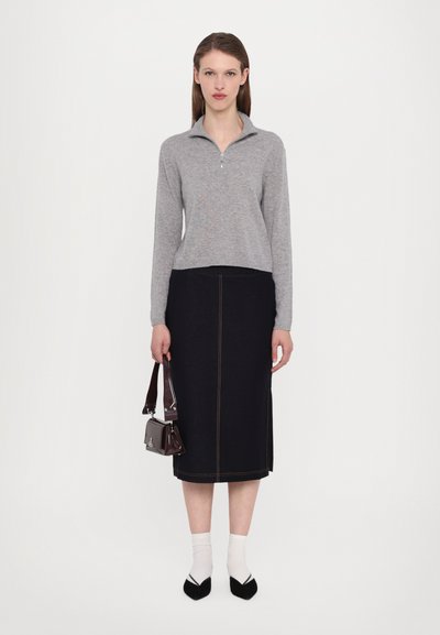 Szürke cipzáras pulóver, sötét farmer szoknya arany varrással, fehér bokazokni, fekete hegyes orrú cipők, és egy kis barna handbag.