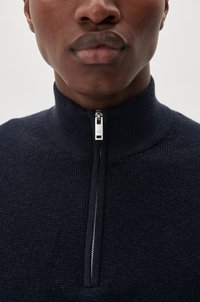 Pullover navy cu fermoar, cu guler înalt, dintr-un material tricotat texturat, și fermoar argintiu având un mic logo pe tab-ul de tragere.
