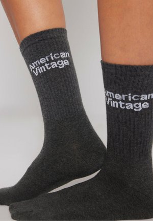 Grå ribbede sokker med hvid "American Vintage" tekst. Materiale af bomuldsblanding, midt på læggen længde, og en glat tekstur med minimal detaljering.