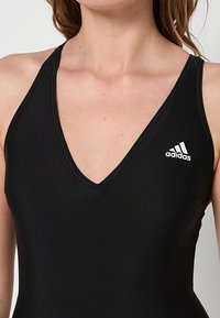 Costume da bagno sportivo nero con scollatura a V profonda. Realizzato in materiale morbido e elasticizzato, presenta un piccolo logo Adidas bianco sul lato sinistro.