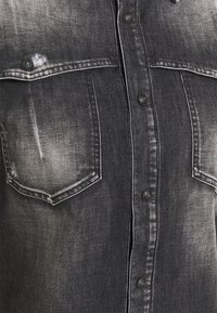 Zwart denim overhemd met een vervaagde finish, voorzien van drukknoopsluiting, twee borstzakken en contrasterende stiksels. Getextureerde stof.
