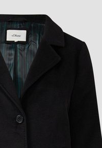Zwarte wollen blazer met een aangeknipte kraag, enkele knoopsluiting en een gestreepte voering in tinten teal. Etiket zichtbaar in het nekgebied.