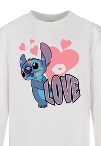 Camicia bianca a maniche lunghe con un personaggio dei cartoni animati dalla pelle blu, grandi orecchie, circondato da cuori rosa e la parola "AMORE" in caratteri in grassetto.