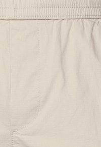 Primer plano de unos pantalones de baño beige con cintura elástica y costuras visibles a lo largo de las costuras laterales y de la cintura.