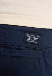 Pantalon bleu marine avec une étiquette portant "Petrol Ind" et "DENIM DRIVEN SINCE '69 FLORIDA U.S.A." Coutures visibles et détails de poche.