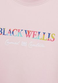 Sweatshirt rose avec "BLACK WELLIS" écrit en lettres colorées et "Casual Couture" brodé en blanc sur le devant. Texture de tissu lisse.
