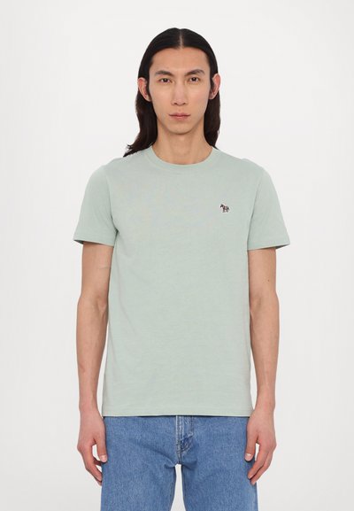 Tricou de bumbac verde deschis, cu mâneci scurte, gât rotund, și un mic logo brodat cu un cal pe piept, asortat cu blugi albaștri.