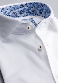 Weißes Baumwollhemd mit klassischem Kragen, ausgestattet mit einem blauen Blumenmuster im Innenfutter und beigen Akzenten, zwei Knopfverschlüssen unterhalb des Kragens.