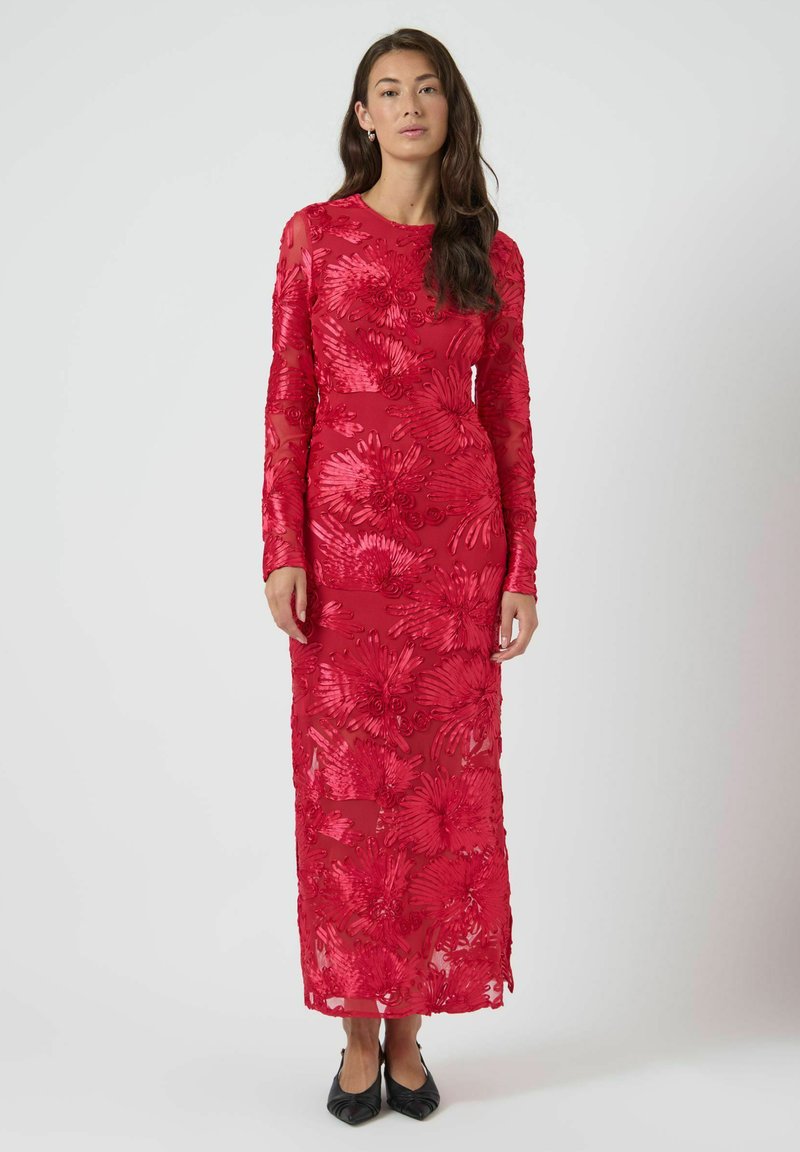Lang rød kjole med blomsterbroderi, gennemsigtig overdel, lange ærmer og figursyet silhuet. Kombineret med sorte balletsko.