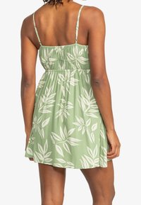 Vihreä, hihaton mekko, jossa on valkoisia lehtikuvioita, rypistetty vyötärö ja säädettävät olkaimet. Kevyt materiaali ja laineileva muoto.