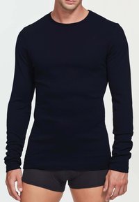 Maglietta nera a maniche lunghe in morbido tessuto, con colletto rotondo e design aderente, abbinata a pantaloni corti scuri. Tessuto liscio, senza motivi.