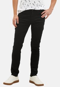 Černé džíny s úzkým střihem a mírným elastanem. Nosit s bílým tričkem s potiskem a bílými teniskami s hnědými podrážkami.