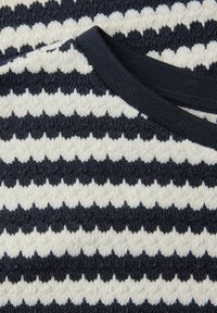 Nærbillede af marineblåt og hvidt tekstureret strikket stof med vandrette zigzagstriber og en ribstrikket kravekant.