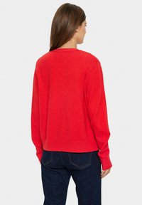 Röd stickad tröja med en avslappnad passform, som har rund halsringning och långa ärmar. Sömmen är något kortad och visar en slät textur.