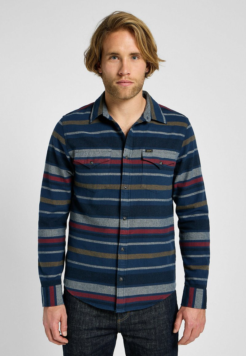 Camicia flanella a bottone in navy con strisce orizzontali grigie, rosse, verdi e beige. Presenta due tasche sul petto e un colletto.