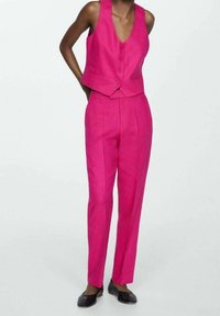 Jasnoróżowa bezrękawnik z trzema guzikami, zestawiony z dopasowanymi spodniami. Gładki materiał i wyraźna konstrukcja.