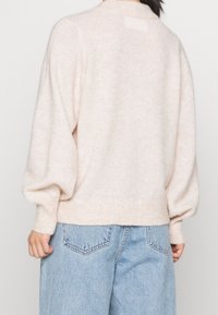 Pull rose clair texturé avec un col montant et des manches ballon, poignets et ourlet côtelés. Porté avec un jean en denim bleu clair taille haute.