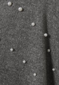 Tessuto grigio lavorato a maglia con accenti di perle bianche sparse. Texture morbida con un motivo sottile, che mostra un mix di fibre chiare e scure.