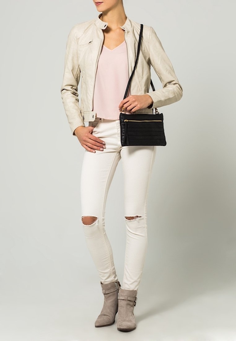 Light beige leather jacket, pale pink top, white ripped skinny jeans, and gray ankle boots, paired with a black textured handbag.