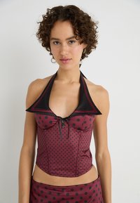 Red and black polka dot halter top with a collar and decorative button detail, made of a smooth, shiny fabric.