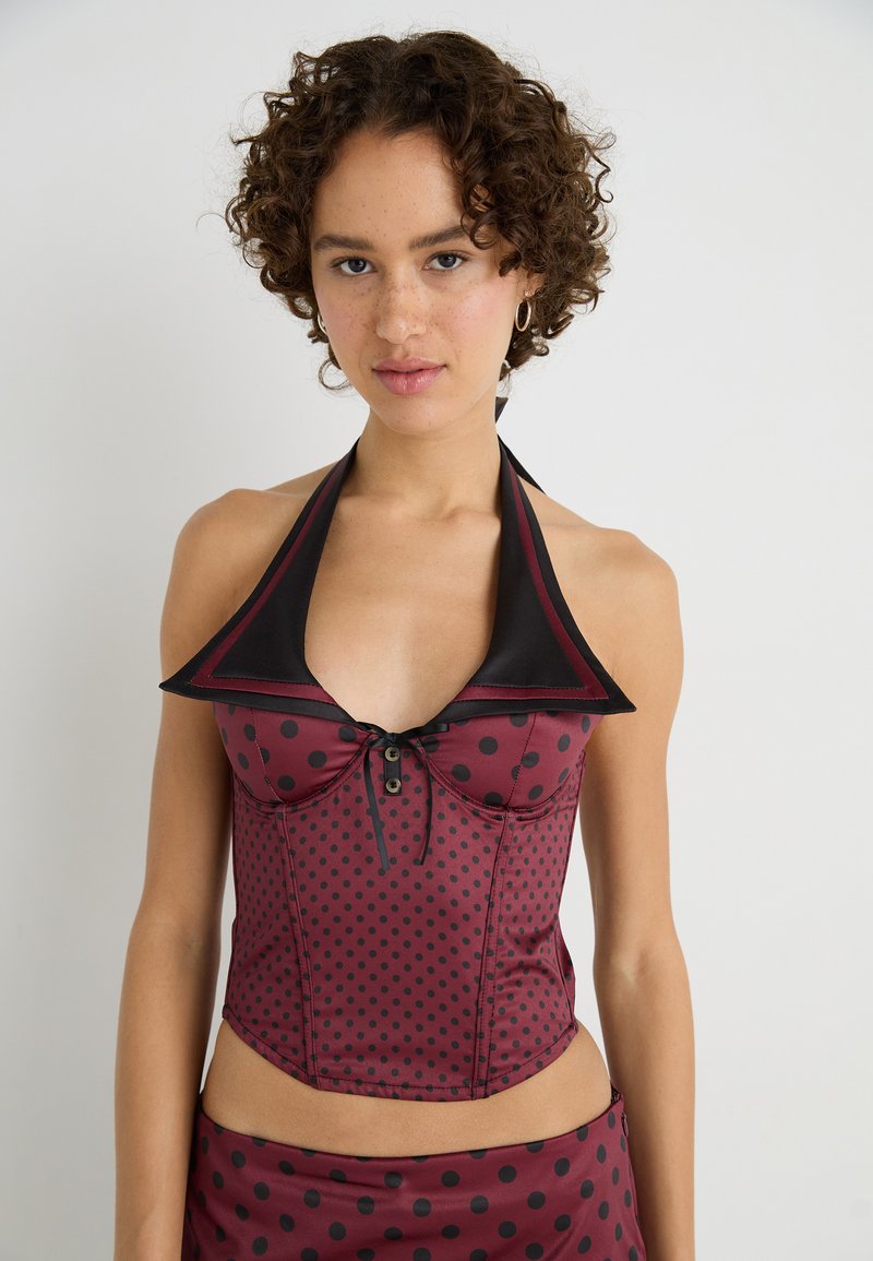 Red and black polka dot halter top with a collar and decorative button detail, made of a smooth, shiny fabric.