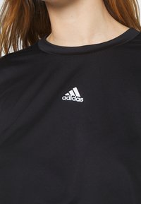 Czarny sportowy t-shirt wykonany z gładkiego materiału, z okrągłym dekoltem i białym logo Adidasa na piersi. Prosty design, krótkie rękawy.