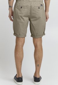 Beige shorts lavet af et struktureret, let stof. Omdrejede afslutninger, elastisk talje og to baglommer med knapper.