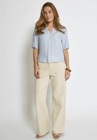 Blusa a maniche corte a righe azzurre e bianche con scollo a V, abbinata a pantaloni beige a gamba larga. Tessuto liscio, design minimalista.