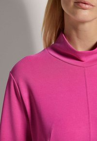 Rosa Rollkragenoberteil aus elastischem Stoff, mit glatter Textur, figurbetonter Form und einer Naht in der Mitte.