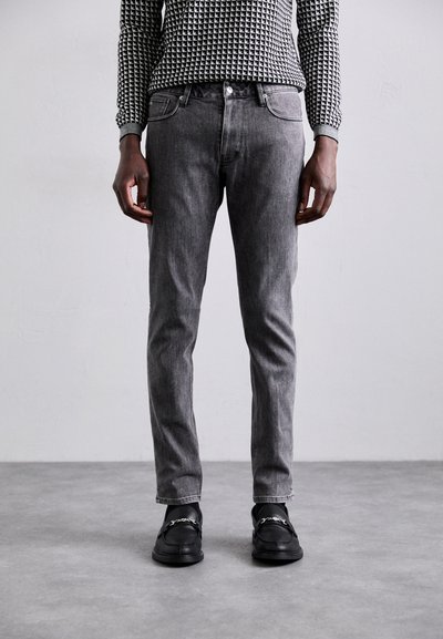 Jeans in denim grigio con vestibilità slim, design a cinque tasche e leggere sfumature. Abbinati a mocassini neri e una maglietta a maniche lunghe con motivo.