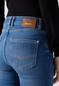 Blauwe spijkerbroek met een hoge tailleband, een bruine leren logo patch en twee achterzakken met decoratieve stiksels.