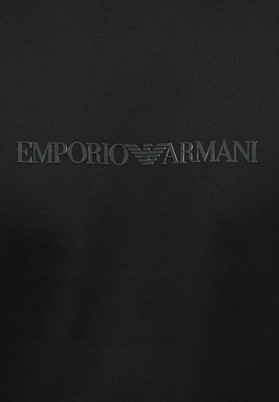 Μαύρο φόντο από ύφασμα με ανάγλυφο σκούρο γκρι κείμενο "EMPORIO ARMANI" και λογότυπο αετού στο κέντρο οριζόντια.