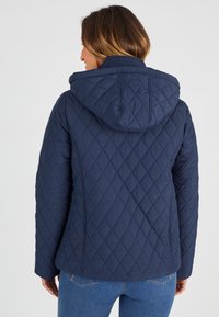Marineblauwe gewatteerde jack met een capuchon, met diamantpatronen en lange mouwen, van achterzijde getoond. Het materiaal lijkt glad en synthetisch.