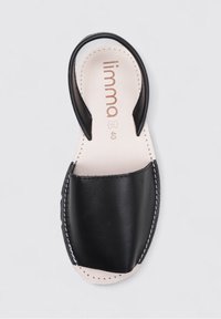 Sandalia de cuero negra con un talón curvado abierto, suela plana y costuras laterales. Presenta un acabado suave y un diseño minimalista. Talla 40.
