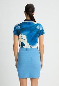 Polo a maniche corte con motivo astratto blu, abbinato a una gonna aderente azzurra. La gonna presenta due tasche posteriori e un passante per la cintura.