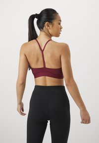 Burgundy sportbh med racerback-design, tillverkad av ett glatt tyg. Bh:n har justerbara axelband och en bred band i nederkant.