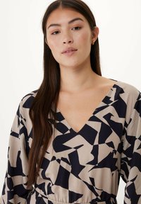 Béžové šaty s výstřihem do V a abstraktním námořnickým vzorem, s dlouhými rukávy a elastickým pasem pro uvolněný střih. Hladká textilie.