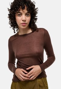 Haut marron à manches longues en tissu léger et transparent, avec un col rond et une coupe ajustée, associé à un pantalon vert olive.