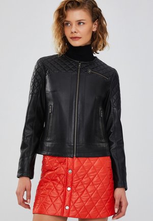 Black leather jacket with quilted upper section, front zippers, and high collar, paired with a red quilted mini skirt featuring snap buttons.