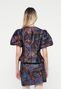 Top s volánovými rukávy a upnutou sukní z iridescentní černé látky s barevnými abstraktními vzory, strukturovaným povrchem a detaily peplum.