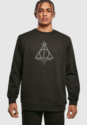Svart hettegenser med hvit grafisk design av en trekant med en sirkel og linjer, tekst "Deathly Hallows" under, ribbestrikkede mansjetter og fald.