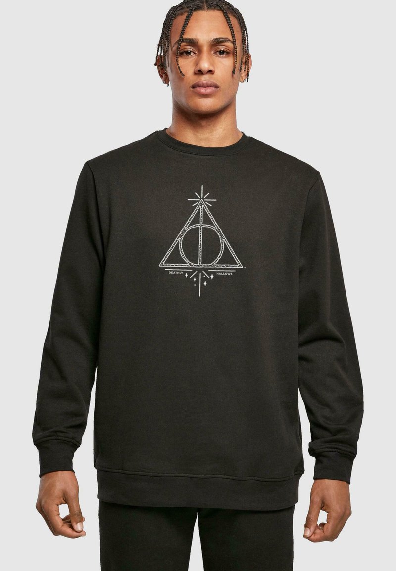 Svart hettegenser med hvit grafisk design av en trekant med en sirkel og linjer, tekst "Deathly Hallows" under, ribbestrikkede mansjetter og fald.