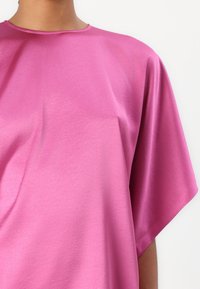 Lyserød satinbluse med afslappet pasform, rund halsudskæring og korte ærmer. Stoffet har en glat, blank tekstur.